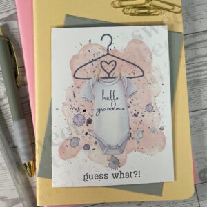 Cute peach pink new baby greeting card announcement featuring onsie with text "hello grandma" and below "guess what?!"