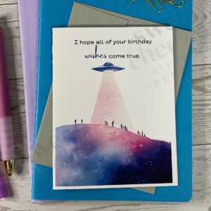 greeting card featuring message "I hope all of your birthday wishes come true" and a UFO shining a light onto the people on a mountain side.