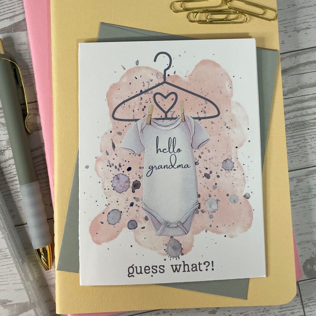 baby onsie with message "hello grandma" clothespin to a hanger and message below that says "guess what?!" cute baby announcement greeting card