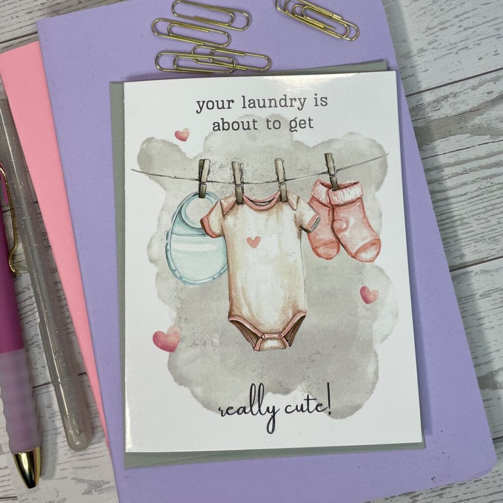 Greeting card featuring baby clothes hanging from a line with clothespins and a onsie, pair of socks and a bib